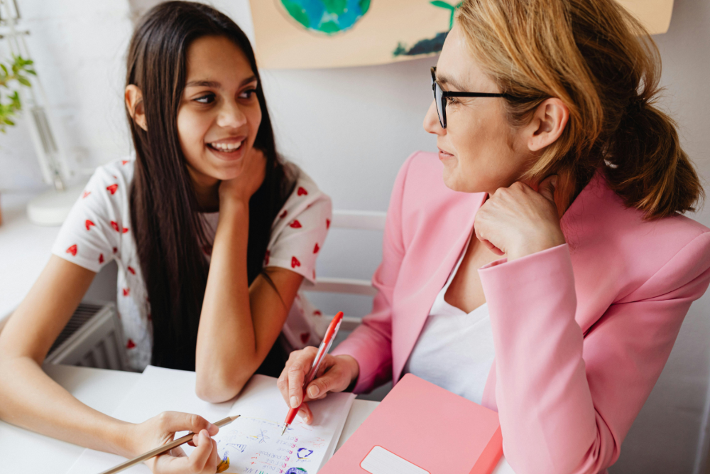 student and tutor smiling at each other while sitting at a desk